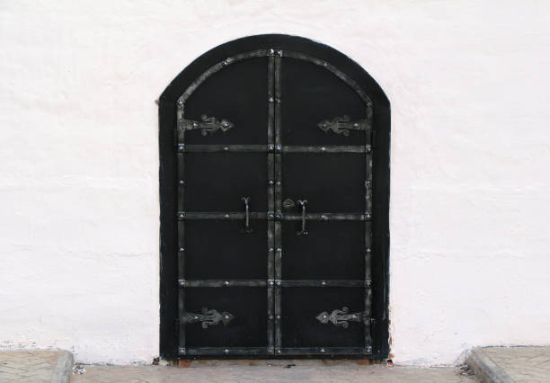 istock Medieval old black door with metal decoration on white wall 1024616368