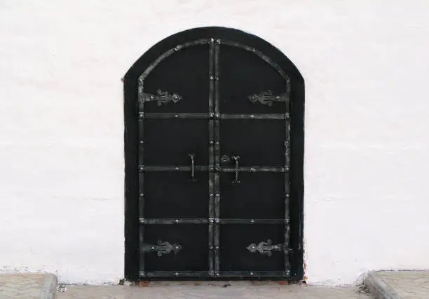 Medieval old black door with metal decoration on white wall