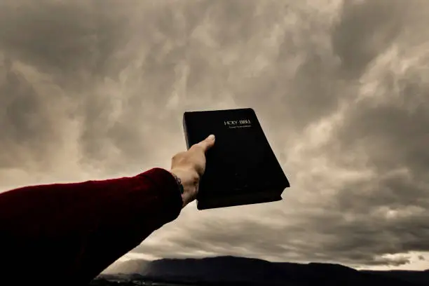 Hand holds bible towards dark sky