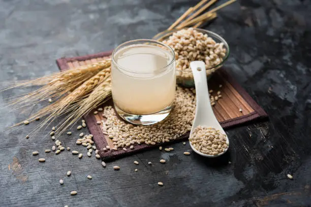 Photo of Barley water in glass with raw and cooked pearl barley wheat/seeds. selective focus