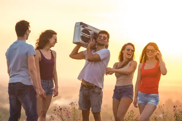 Photo of The young people stand with a boom box on the bright sun background