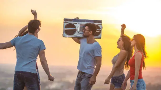 Photo of The young people dancing with a boom box on the sunset background