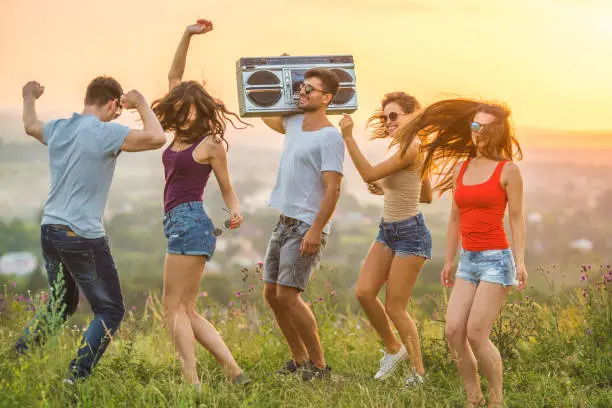 Photo of The five people dancing with a boom box on the sunset background