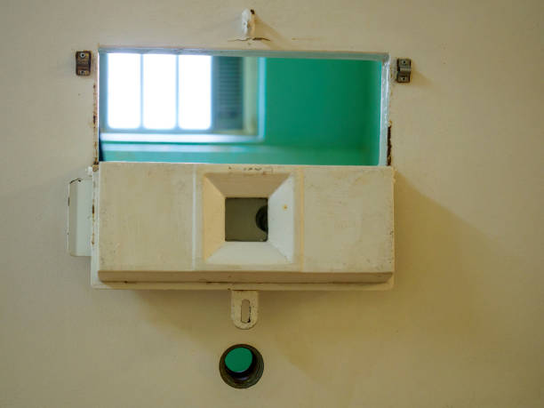 An open peep hole looking into a cell in a disused prison
