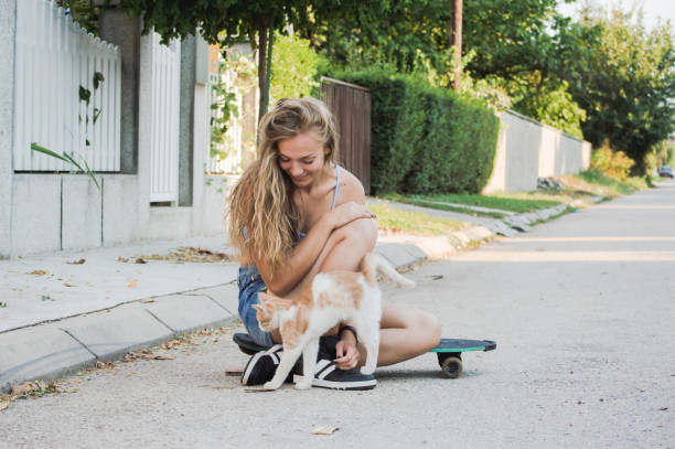 Attractive blond girl sitting on skateboard on the street and playing with kitty