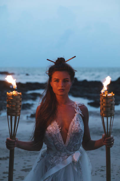 istock Bride in beautiful wedding dress is holding torchlight on the beach 1024670886