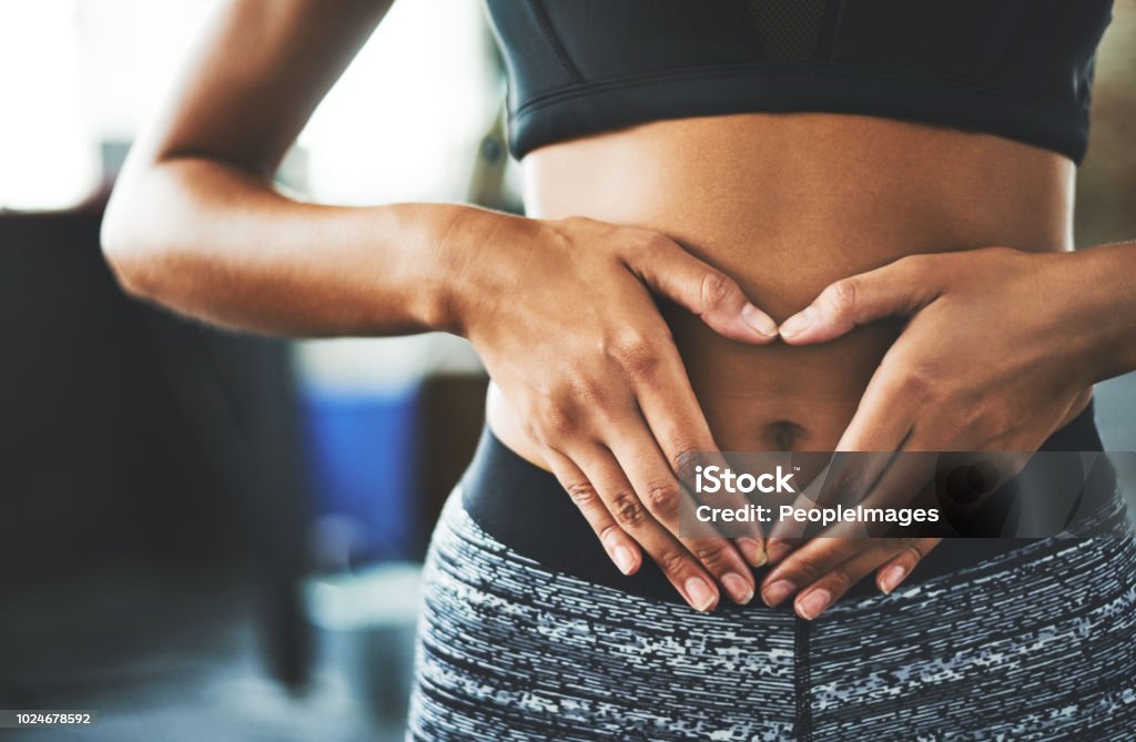 Everyday is core strengthening day Cropped shot of a fit young woman making a heart shaped gesture over her stomach in a gym Abdomen Stock Photo