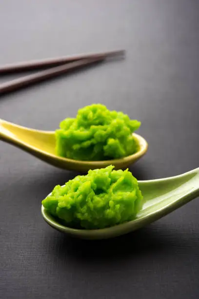 Photo of Green wasabi sauce or paste in bowl, with chopsticks or spoon over plain colourful background. selective focus