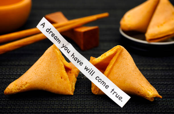 istock Paper strip with phrase A Dream You Have Will Come True from fortune cookie, another cookie and chopsticks on black napkin background. 1024692992