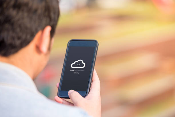 istock Cloud uploading concept on phone screen. Man hold phone doing cloud uploading at the outdoor. 1024709694