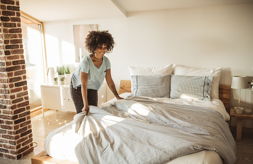 Young woman making bed at home. She is in pajamas. Doing her morning routine.