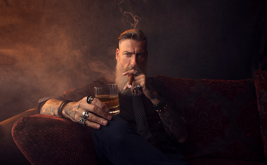 Retrato de un hombre de negocios atractivo con un cigarro y un vaso de whisky en un cuarto oscuro photo