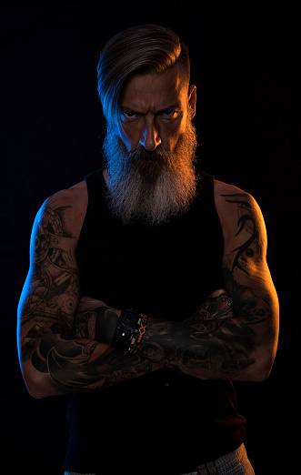 Portrait of an angry bearded man with crossed arms in orange and blue light