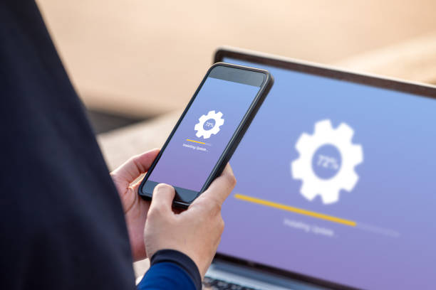 Hijab woman holding smartphone doing installing update process with gearbox percentage progress and loading bar with installing update on screen laptop background stock photo