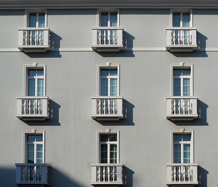 Elegant light grey facade with large windows and small white balconies with columns, in classical style .