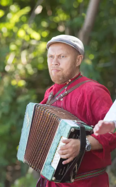 Photo of A man in a Russian national costume playing the accordion on a Slavic holiday