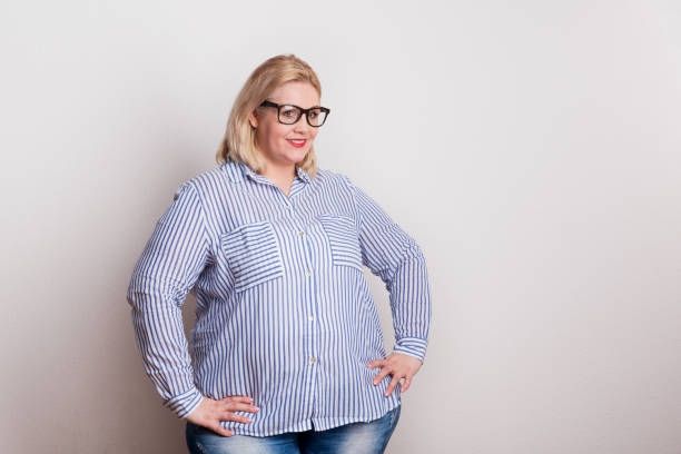 Portrait of an attractive overweight woman with glasses in studio. Portrait of an attractive blond overweight woman with red lips and glasses, arms on hips. Studio shot. big fat lips stock pictures, royalty-free photos & images
