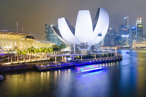 singapur, 27 de octubre de 2015: un barco pasa por delante del centro comercial artscience museum y arenas, frente a marina bay y el distrito financiero, en singapur. - artscience museum fotografías e imágenes de stock