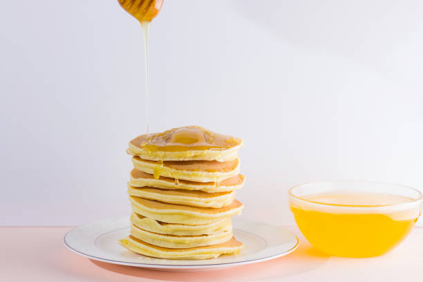 istock Pancakes on a white pink background. Hot pancakes with honey on a white plate with copy space. Delicious dish for breakfast. Honey flows down from a wooden stick on a dish 1024805326