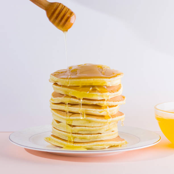 istock Pancakes on a white pink background. Hot pancakes with honey on a white plate with copy space. Delicious dish for breakfast. Honey flows down from a wooden stick on a dish 1024805364
