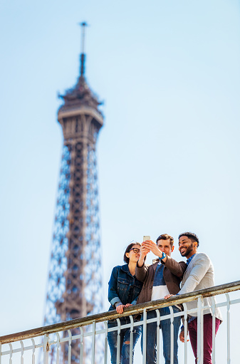 Three young tourists visiting Paris, taking a selfie with the Eiffel Tower in the background.