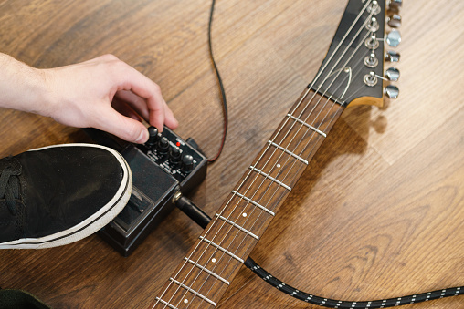 Man with musical instrument setting up guitar audio stomp box effects and cables in music studio