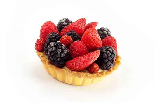 Closeup of cream custard small tart, decorated with strawberries and blackberries, isolated on white background.
