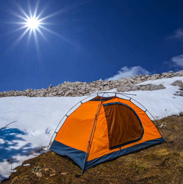 closeup orange touristic tent on the snowbound mount slope under a sparkle sun