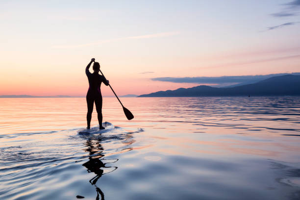 Sunset Paddle Adventurous girl on a paddle board is paddeling during a bright and vibrant sunset. Taken near Spanish Banks, Vancouver, British Columbia, Canada. paddleboard photos stock pictures, royalty-free photos & images