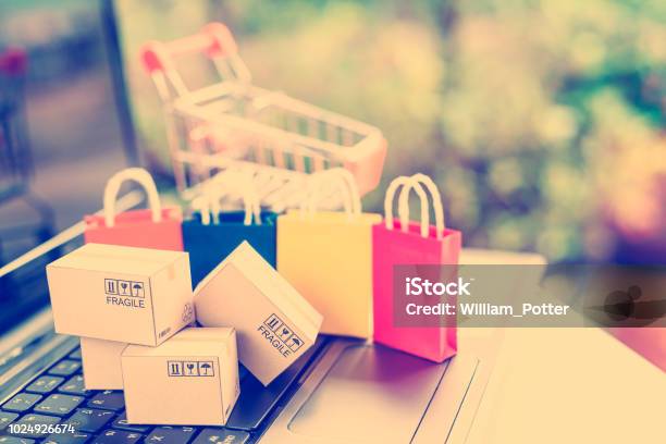 Online Shopping And E Commerce With Delivery Service Concept Paper Boxes Or Cartons On Laptop With A Shopping Cart And Paper Shopping Bags Behind Online Shopping Is Popular Due To Its Convenience Stock Photo - Download Image Now