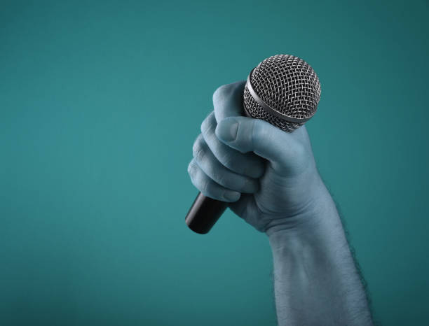 istock Close-Up Of Hand Holding Microphone Against Blue Background 1024942146