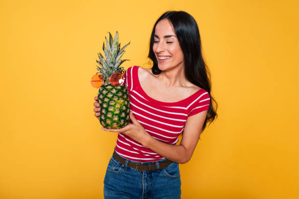 Pineapple summer party. Beautiful young smiling woman with pineapple in hands on orange background