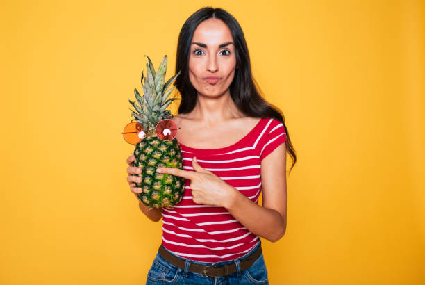 Pineapple summer party. Beautiful young smiling woman with pineapple in hands on orange background