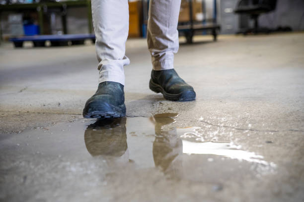 un operaio in un magazzino che cammina nel liquido versato. - wet foto e immagini stock