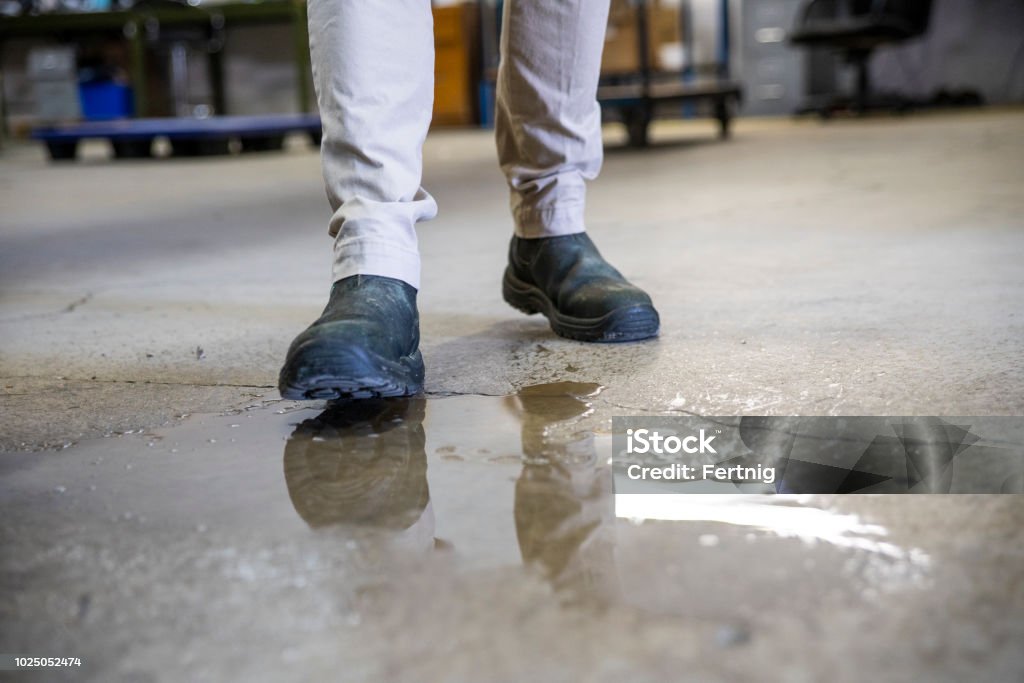 A worker in a warehouse walking in spilled liquid. A male worker wearing work boots in a warehouse walking into a liquid spill on the floor. Flooring Stock Photo