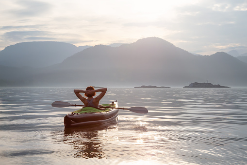 Woman on a kayak is enjoying the beautiful Canadian Mountain Landscape during a vibrant sunset. Taken in Howe Sound, North of Vancouver, British Columbia, Canada.