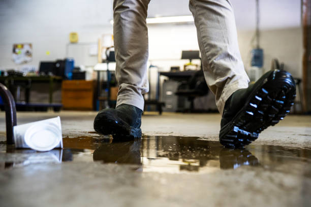 un travailleur dans un entrepôt à pied en liquide déversé. - single drop photos et images de collection