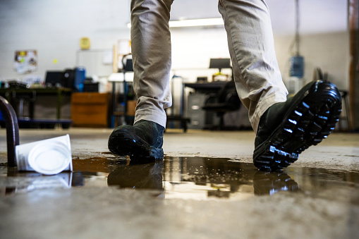 A male worker wearing work boots in a warehouse walking into a liquid spill on the floor.