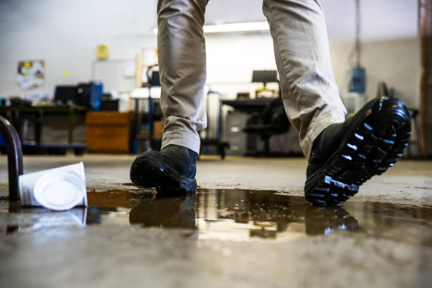 A worker in a warehouse walking in spilled liquid. A male worker wearing work boots in a warehouse walking into a liquid spill on the floor. unsafe workplace stock pictures, royalty-free photos & images