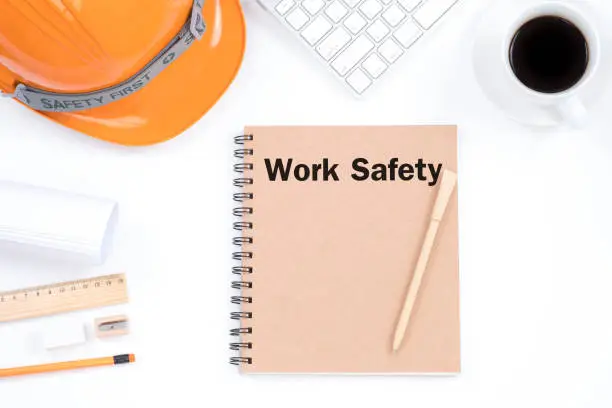 Work safety concept. Top viwe of modern workplace with safety helmet, office supplies, a cup of coffee and keyboard on white background.
