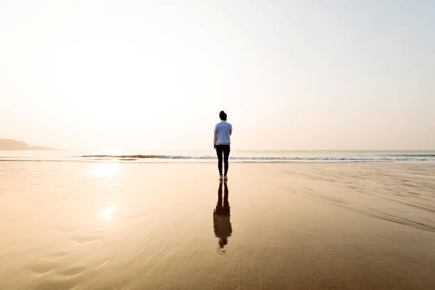 istock Woman standing on the beach at sunset 1025097628