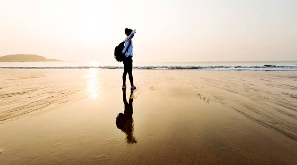 istock Woman backpacker standing on the beach at sunset 1025098052