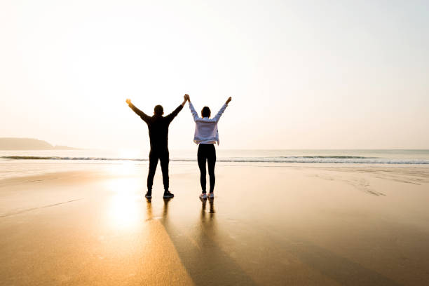 istock Couple standing at beach with arms raised 1025103300