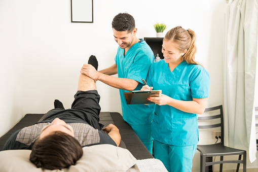 Young physical therapists checking patient's leg and preparing notes in hospital