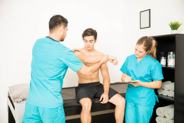 istock Physiotherapist Examining Shirtless Customer's Hand While Coworker Writing Notes 1025148310