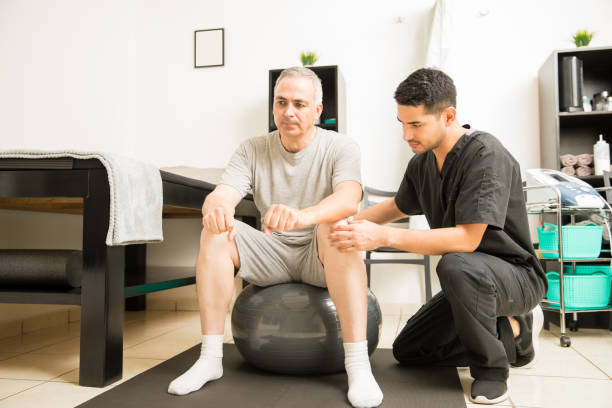 istock Physiotherapist Helping Patient Sitting On Exercise Ball 1025148596