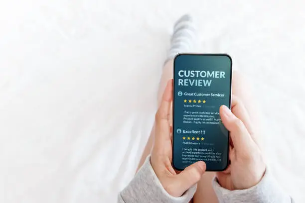 Photo of Customer Experience Concept. Woman lying on Bed to Reading Online Review via Smartphone before Buying Products and Services, More Positive Feedback on Mobile Screen