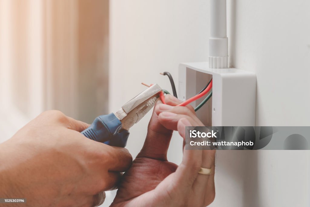 technology in home The technician is using a pliers wrench to install the power plug on the wall. Electricity Stock Photo