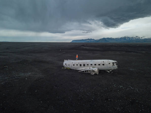 istock DRONE view Young woman stands on airplane crashed on black sand beach looking around her contemplating surroundings 1025336086