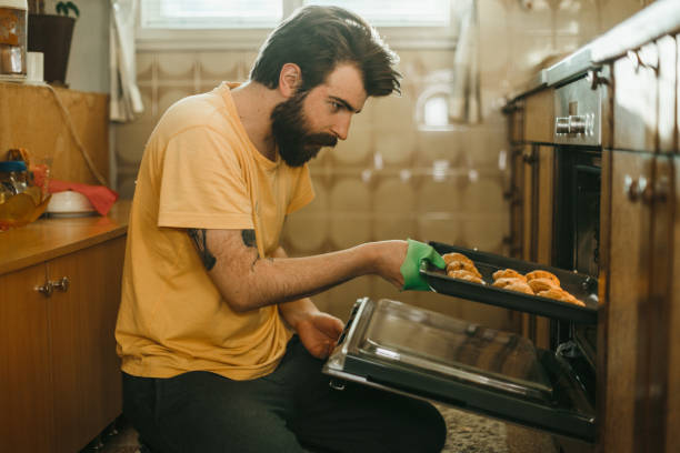 istock Young bearded man taking out freshly baked pastries from the oven 1025372716